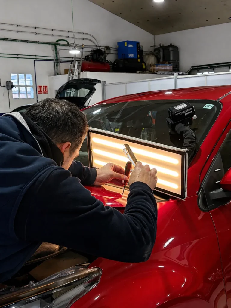 Desabollado sin pintura (PDR) con varillas y lámpara de reflejos en un coche rojo