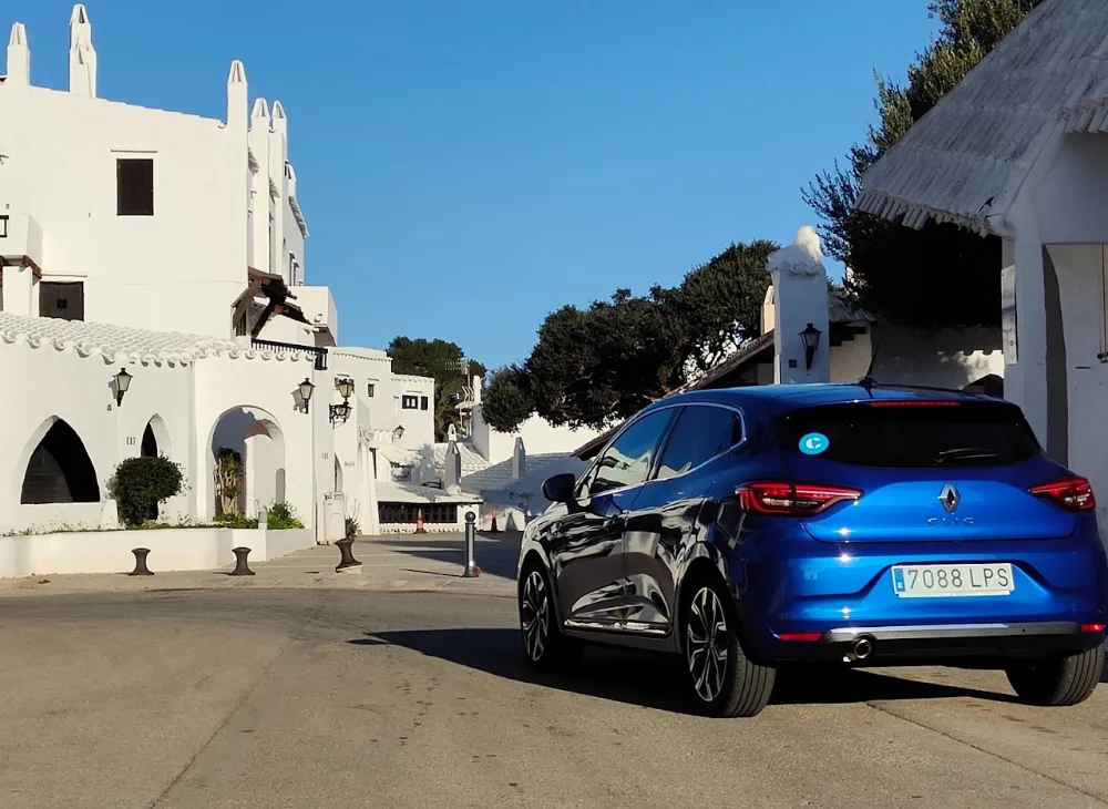 Coche azul de alquiler en un pueblo blanco de Menorca